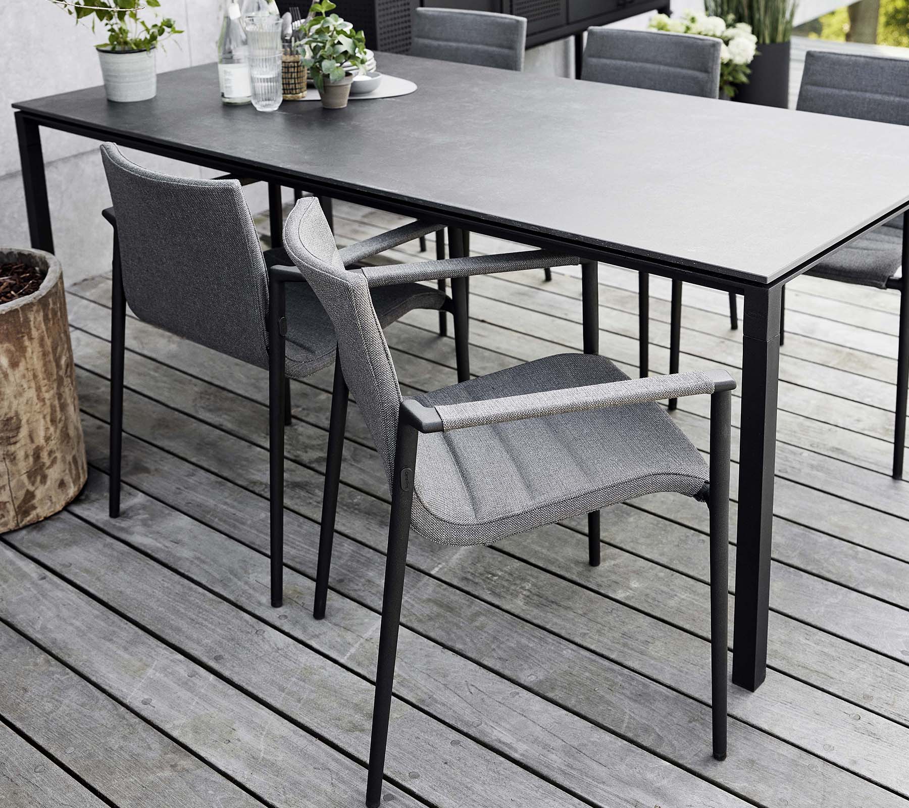 Stilren matplats med ett elegant bord och moderna grå kärnstolar, omgiven av naturliga element och grönska.