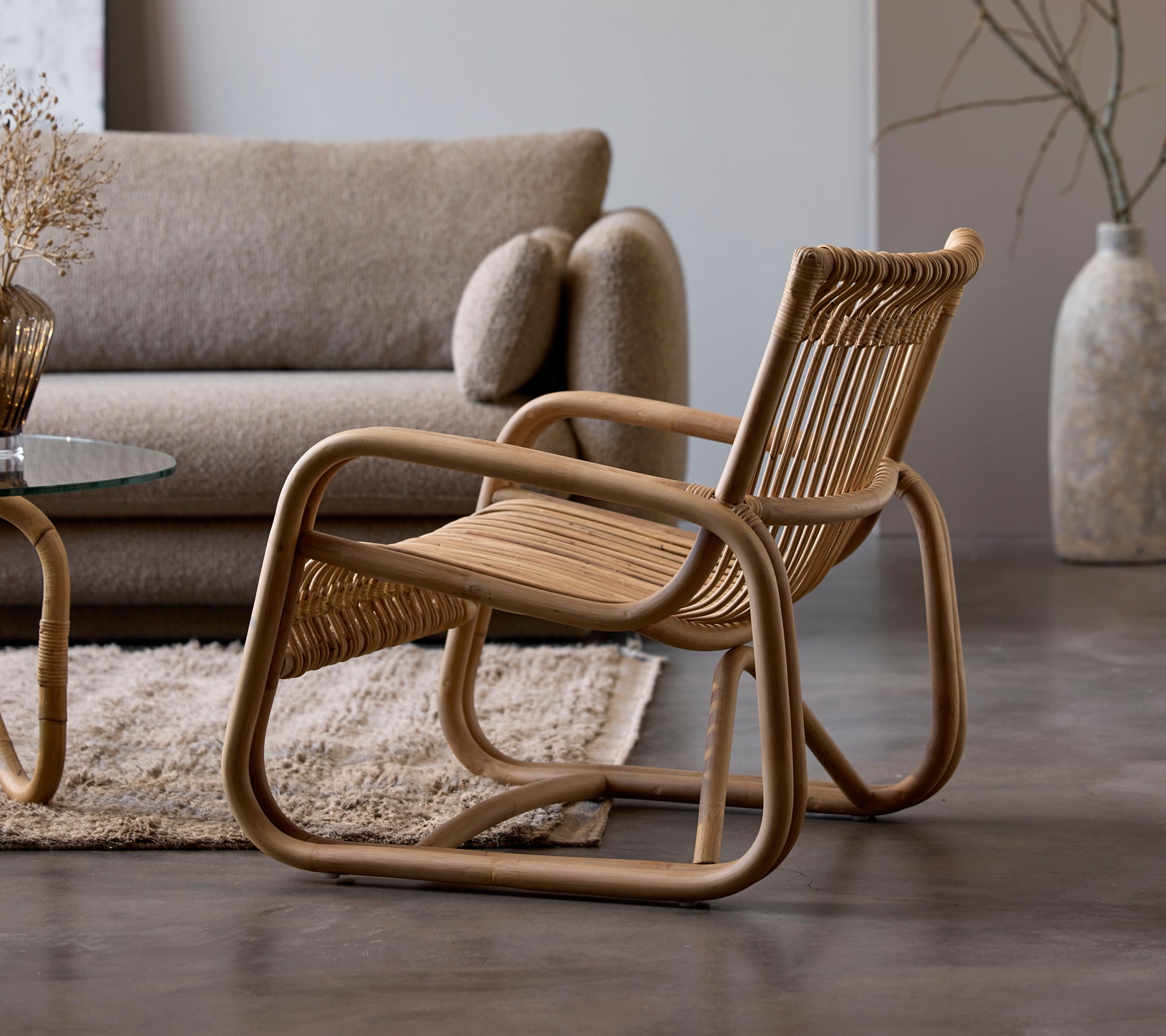 Rattanstol bredvid en beige soffa och ett glasbord i en modern loungemiljö.