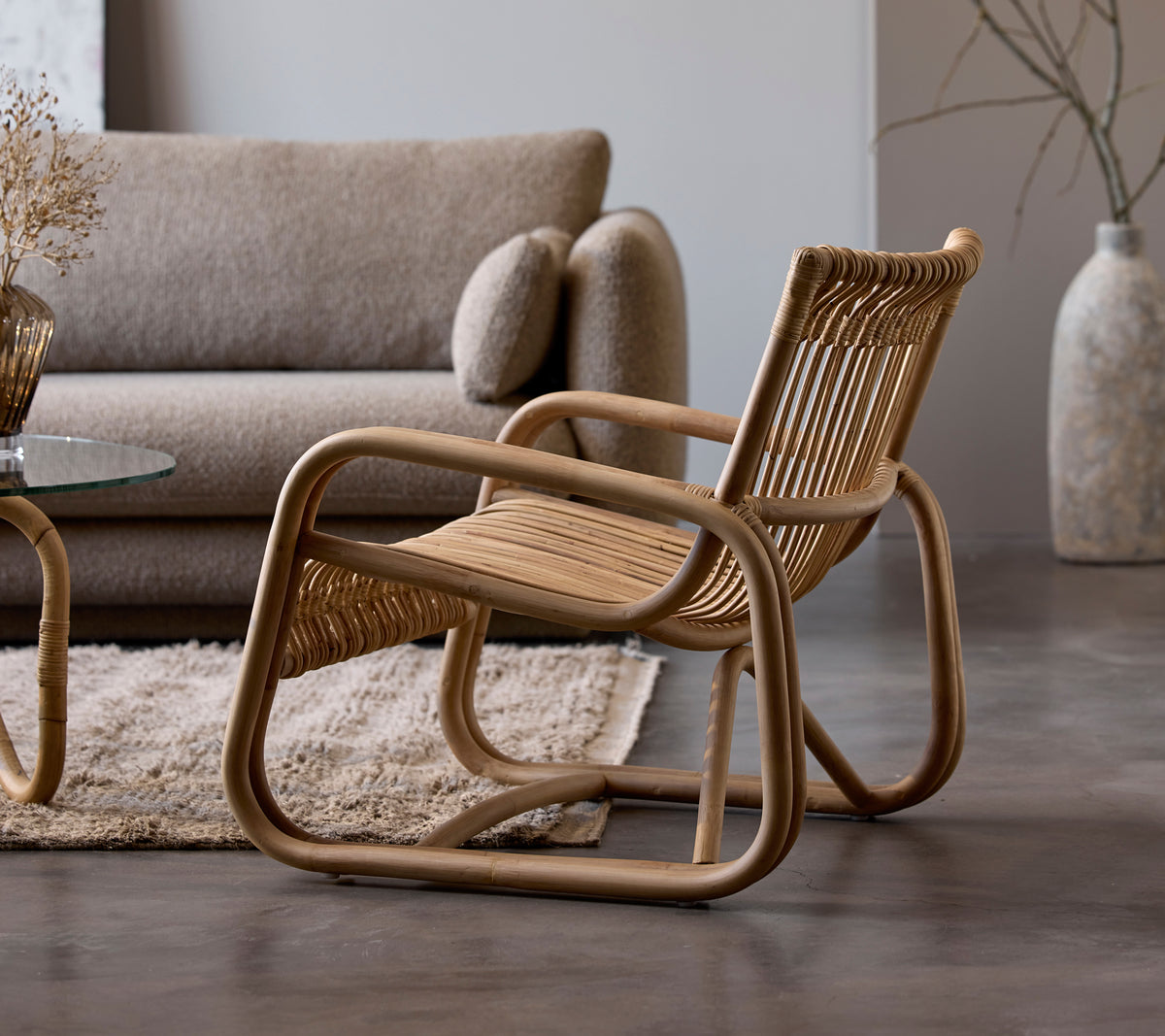 Rattanstol bredvid en beige soffa och ett glasbord i en modern loungemiljö.