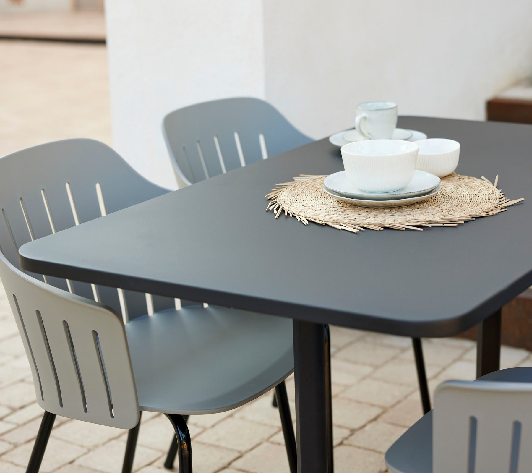 Modernt cafébordset med en svart bordskiva, omgivet av grå stolar, med tallrikar och koppar på en halvmatt.
