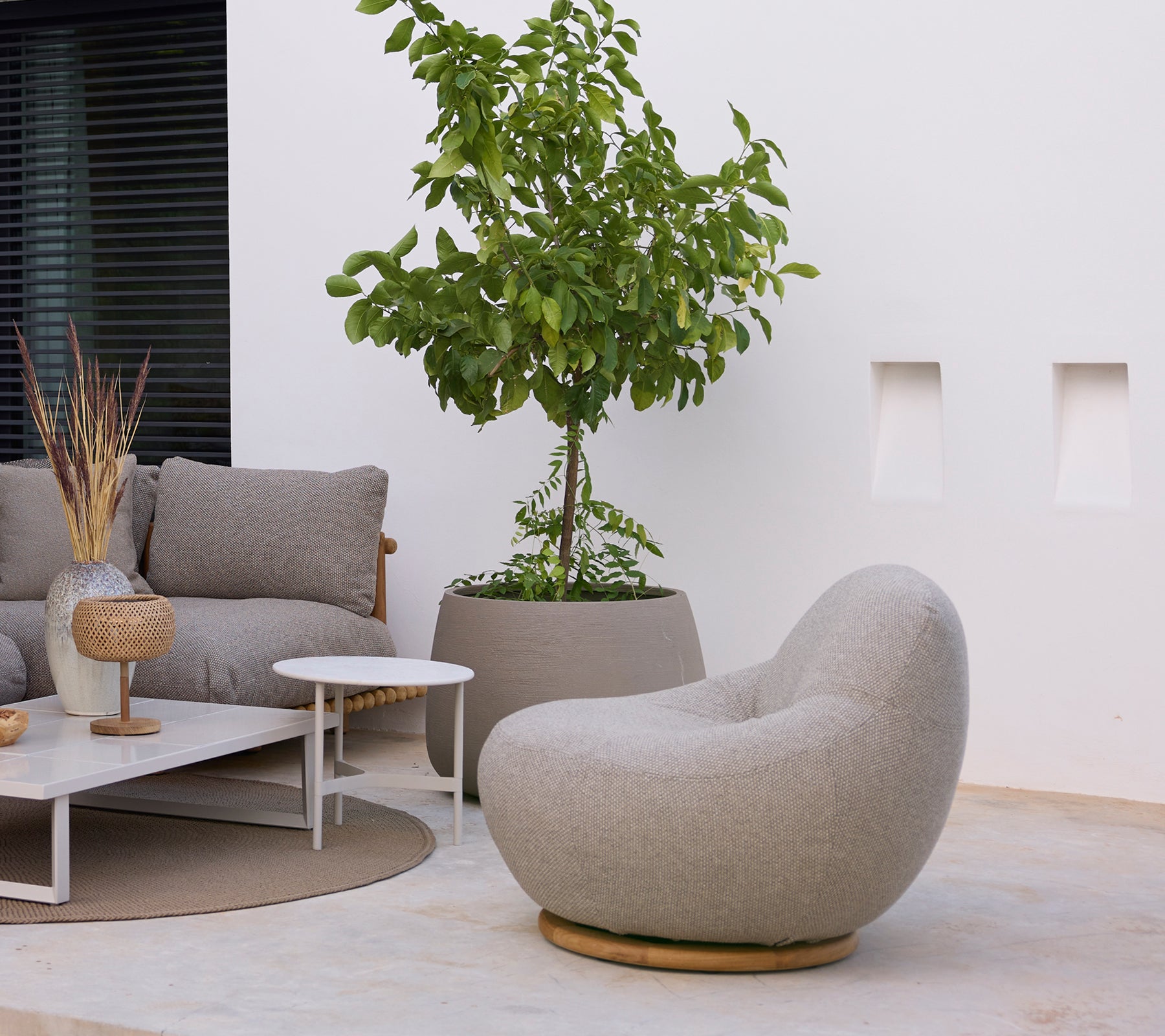 Modern loungeområde med en grå stol, soffa, vitt soffbord och grön växt.