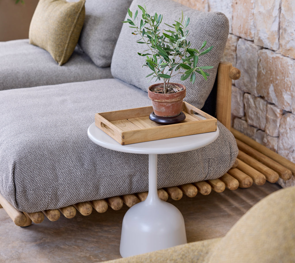 Modern loungemöblering med en grå soffa, ett vitt sidobord och en grön växt.