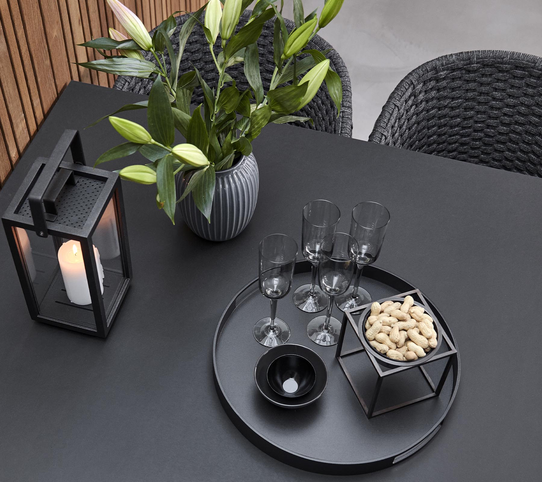En stilren bordsdekoration med en ljuslykta, en vas med blommor, glas och en serveringsbricka med snacks.