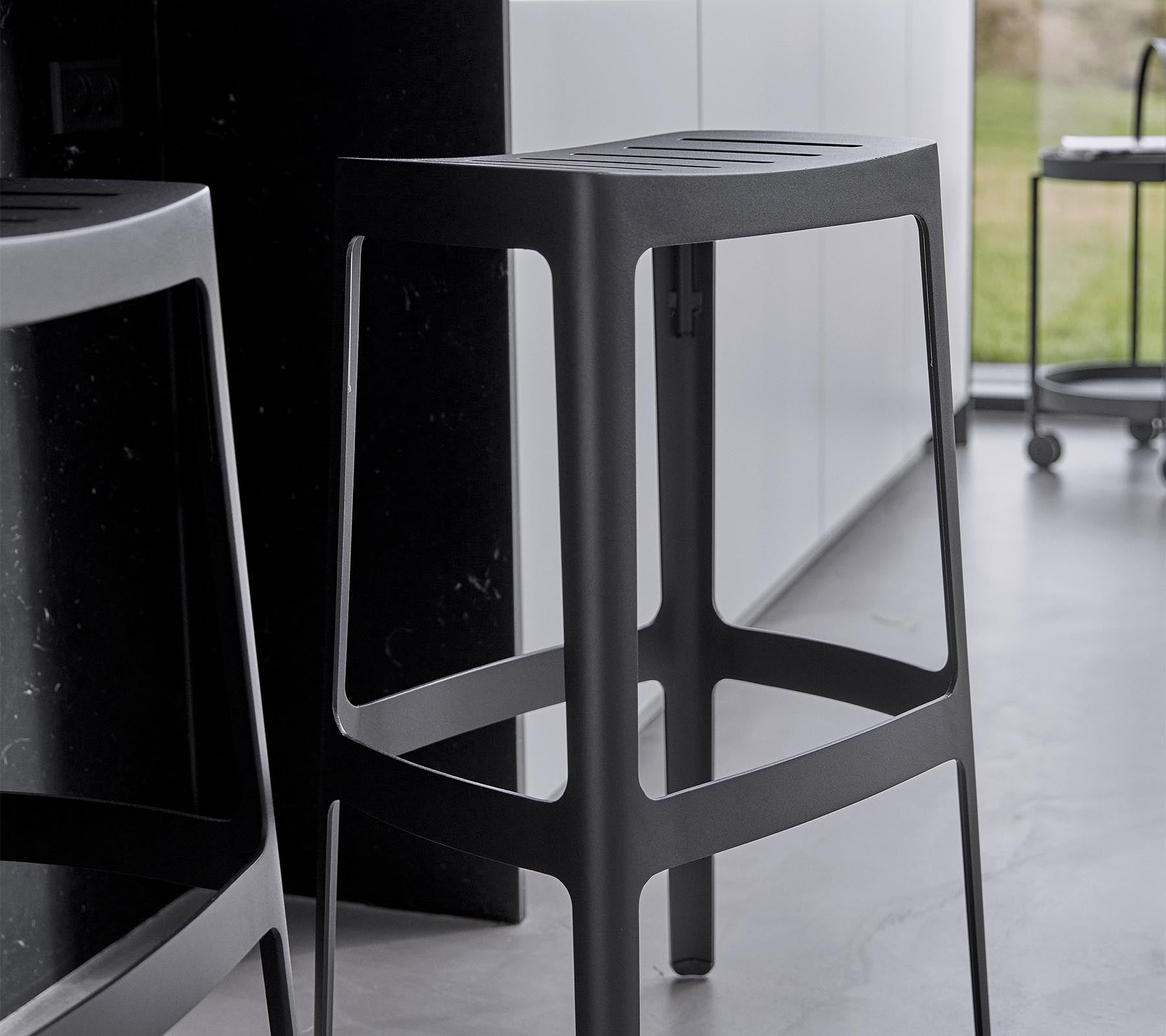En stilren, modern barstol med en minimalistisk design, som har en robust struktur och en elegant svart finish.