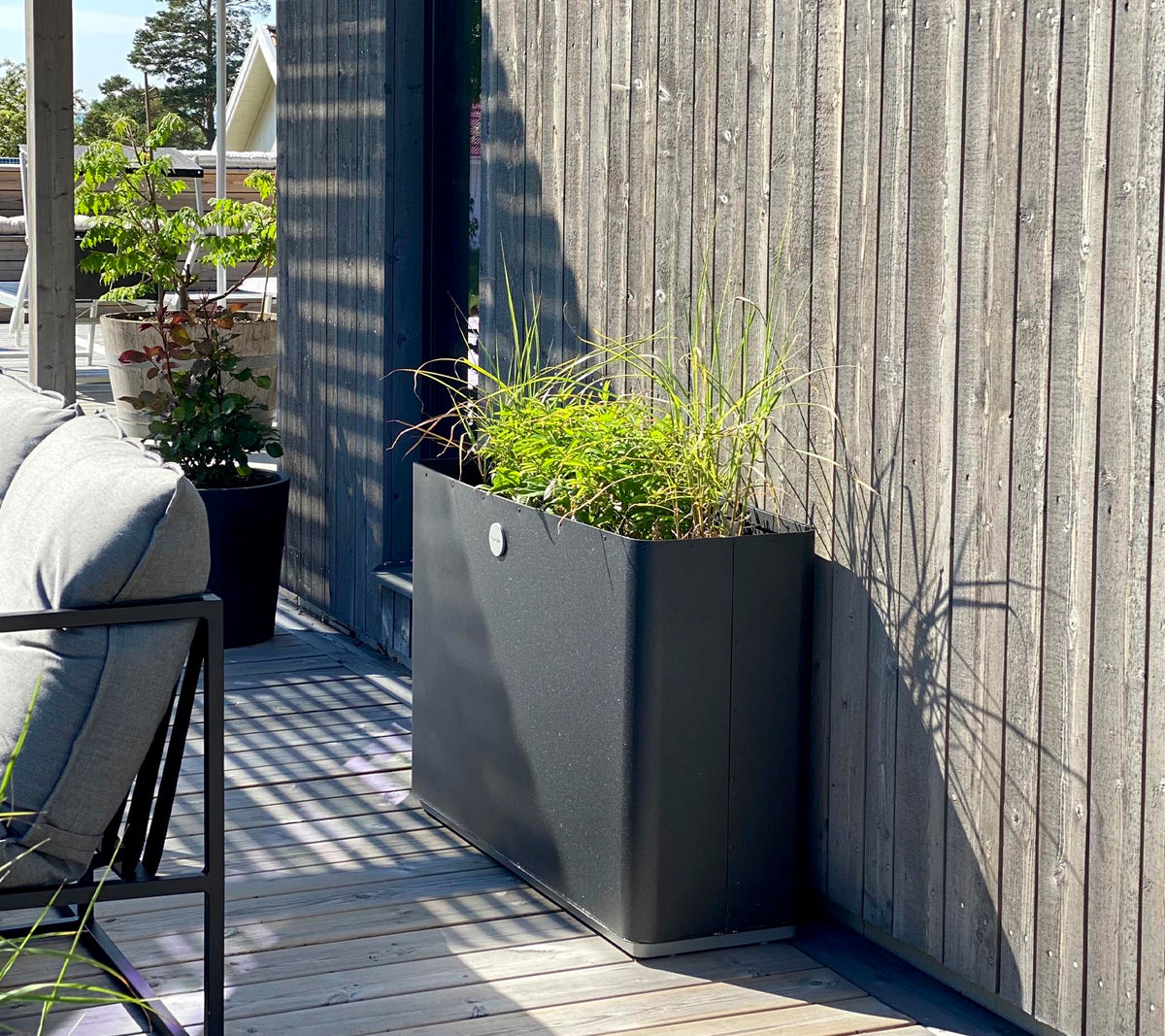En elegant, modern planter med livlig grönska står mot en texturerad trävägg och kompletterar det omgivande rummet.