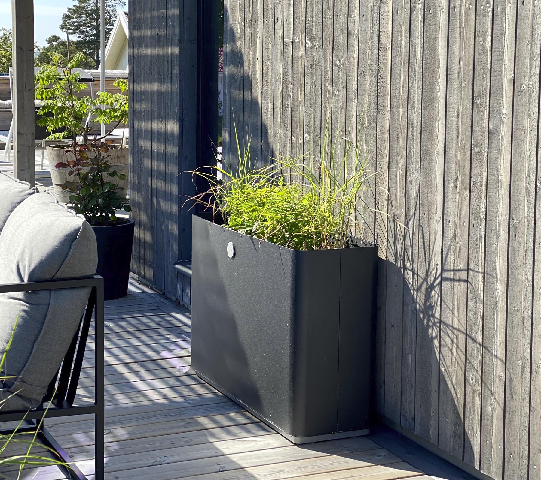 En elegant, modern planter med livlig grönska står mot en texturerad trävägg och kompletterar det omgivande rummet.