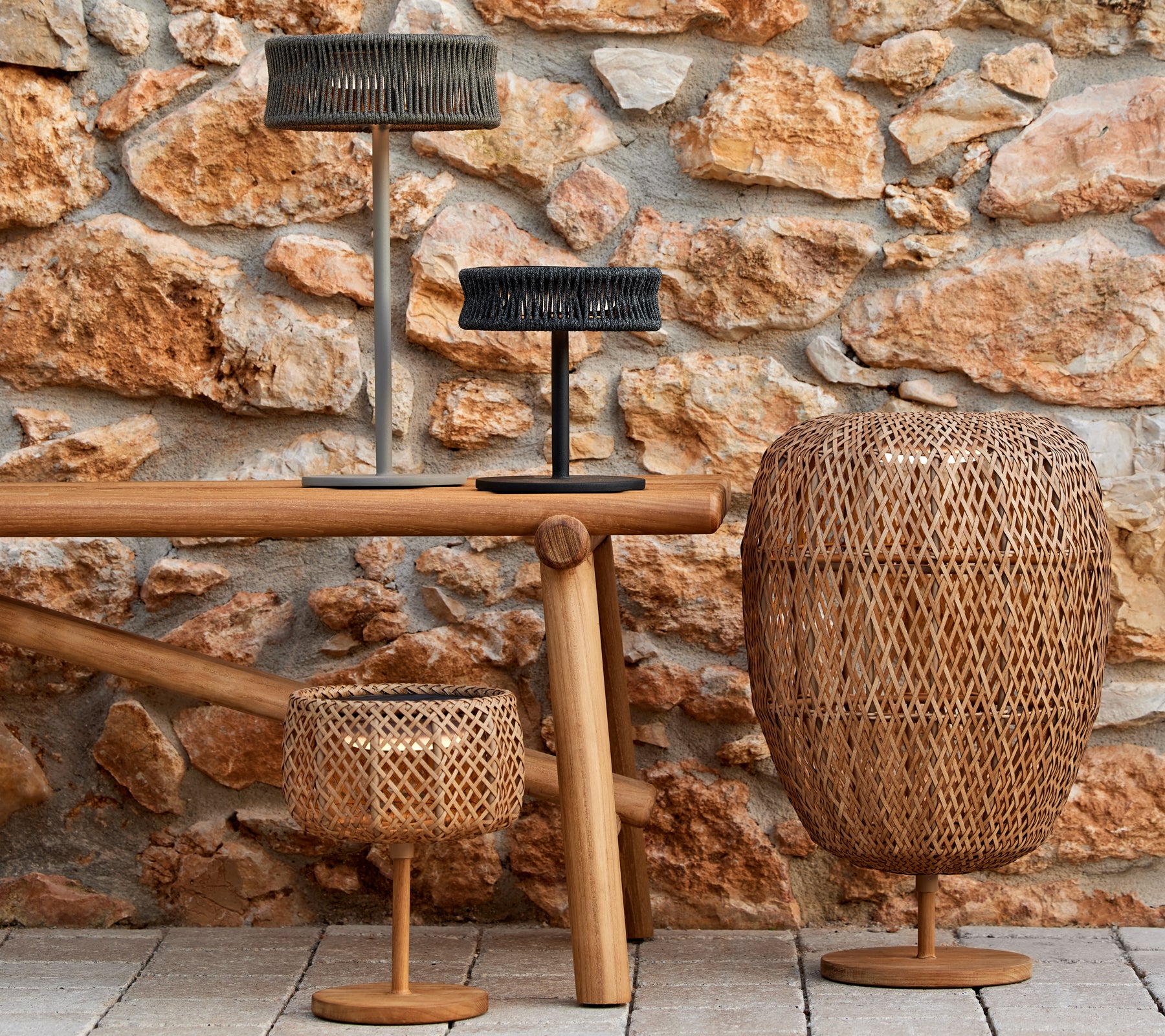 En trio av stiliga vävda lampor i olika storlekar, som framhäver samspelet mellan ljus och textur mot en rustik stenmur.