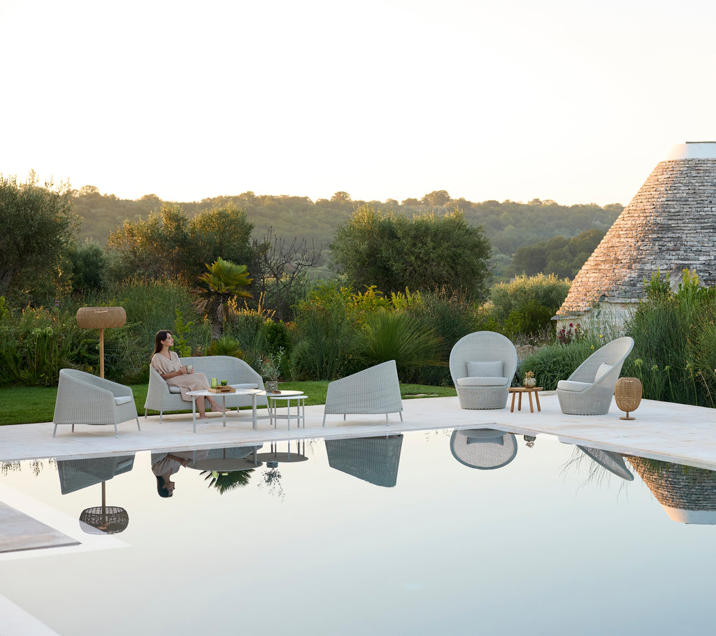 Moderna utomhusloungområdet med grå stolar och ett vitt bord vid en pool.