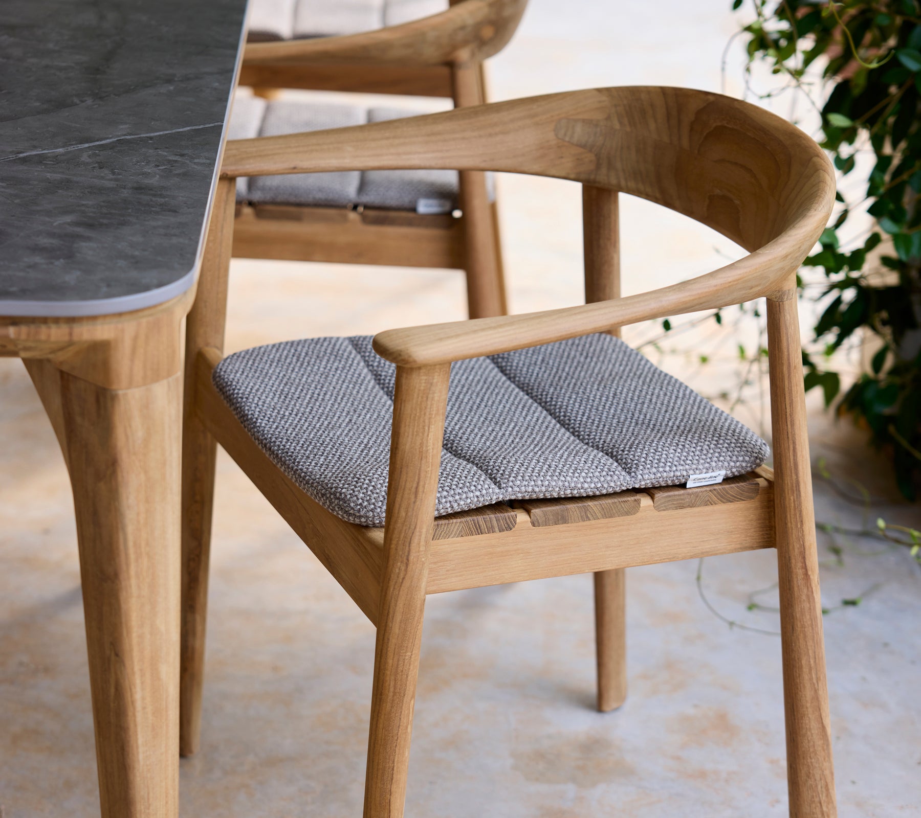 Modern trästol med grå kudde bredvid ett bord i en loungeinställning.