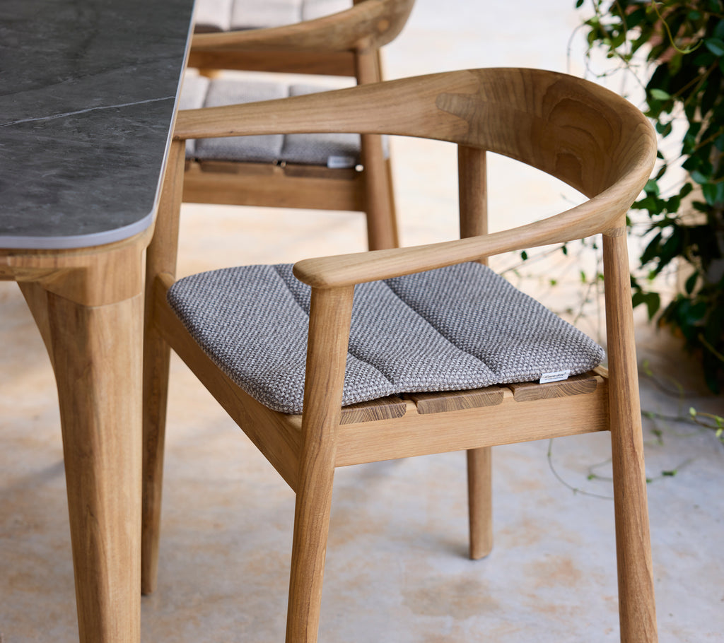 Modern trästol med grå kudde bredvid ett bord i en loungeinställning.