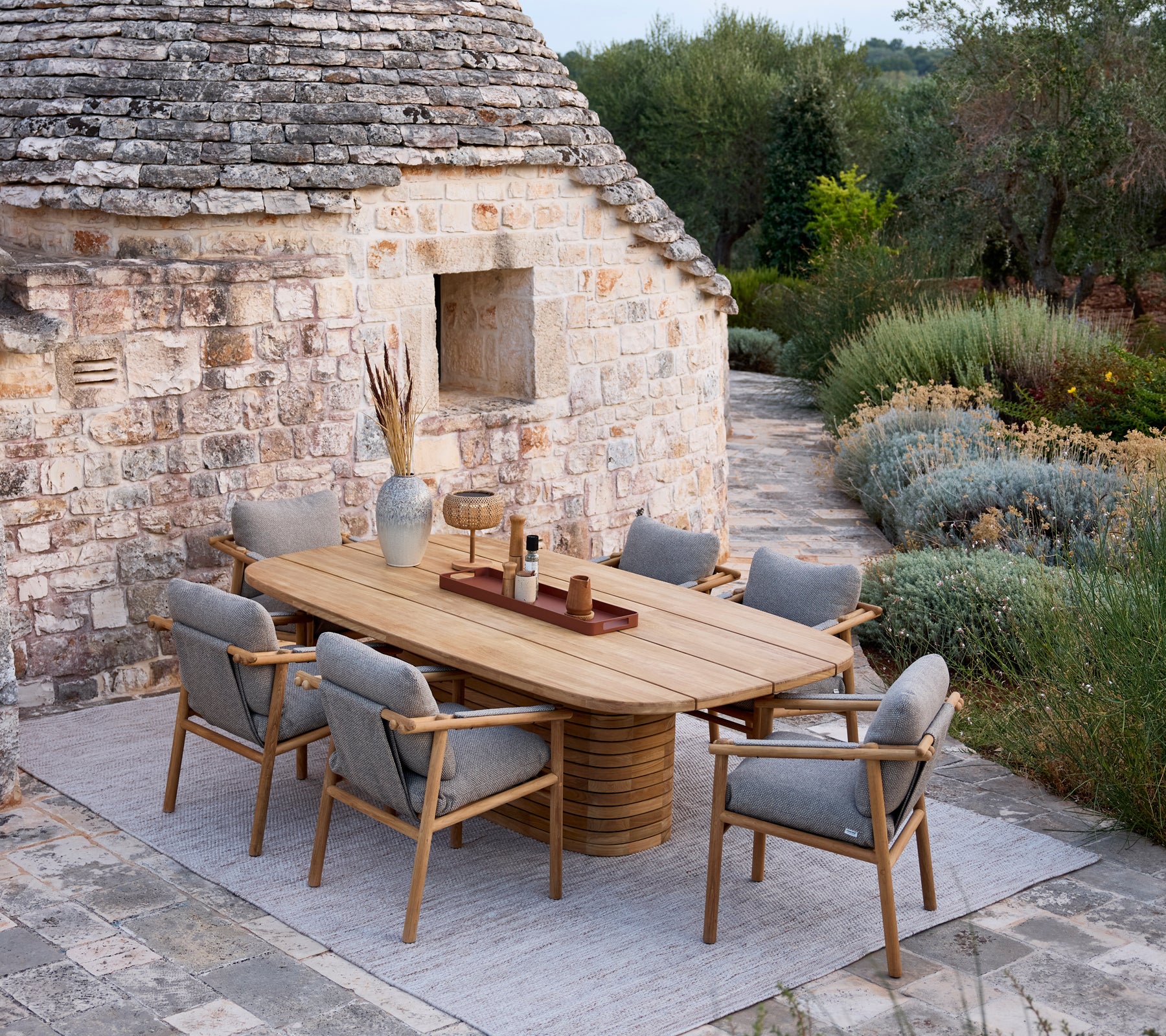 Trämötebord med grå klädda stolar i en rustik utomhusmiljö.