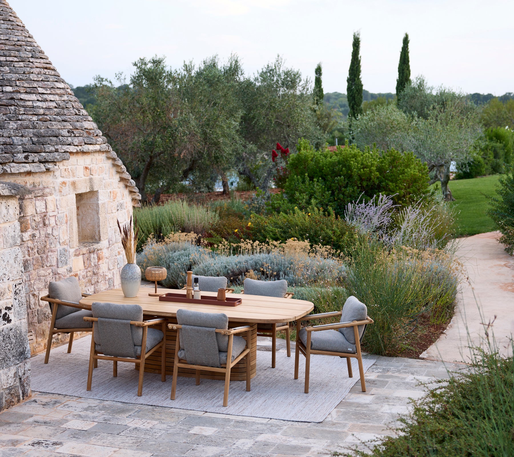 Modern utomhusmatplats med ett runt bord och grå stolar omgiven av grönska.