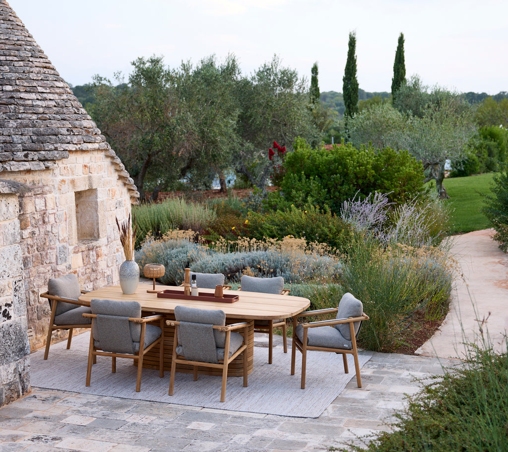 Modern utomhusmatplats med ett runt bord och grå stolar omgiven av grönska.