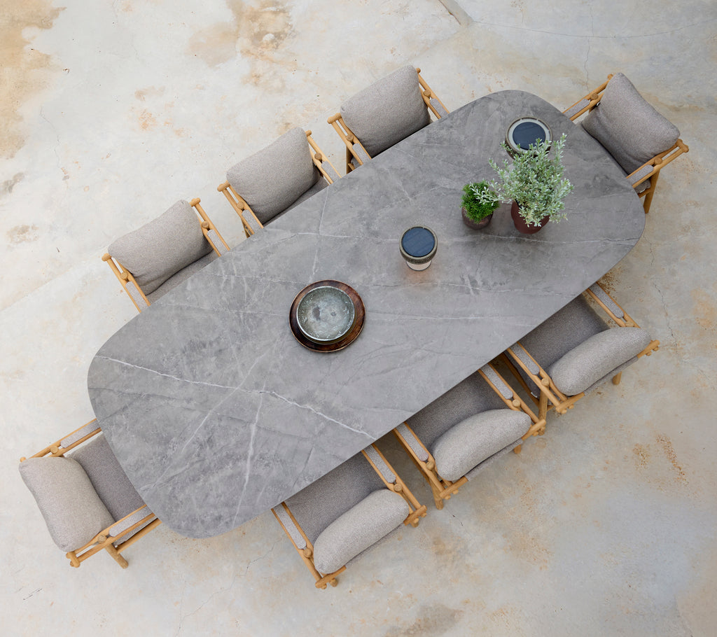 Modern matsituation med ett grått bord, beige kuddar och trästolar.