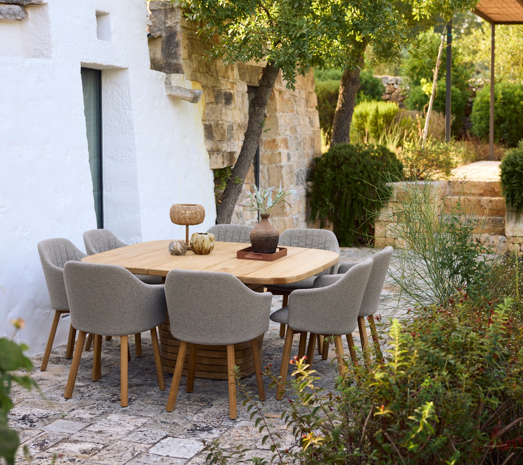 Modernt trä middagsbord omringat av grå stolar i en trädgårdsinställning.