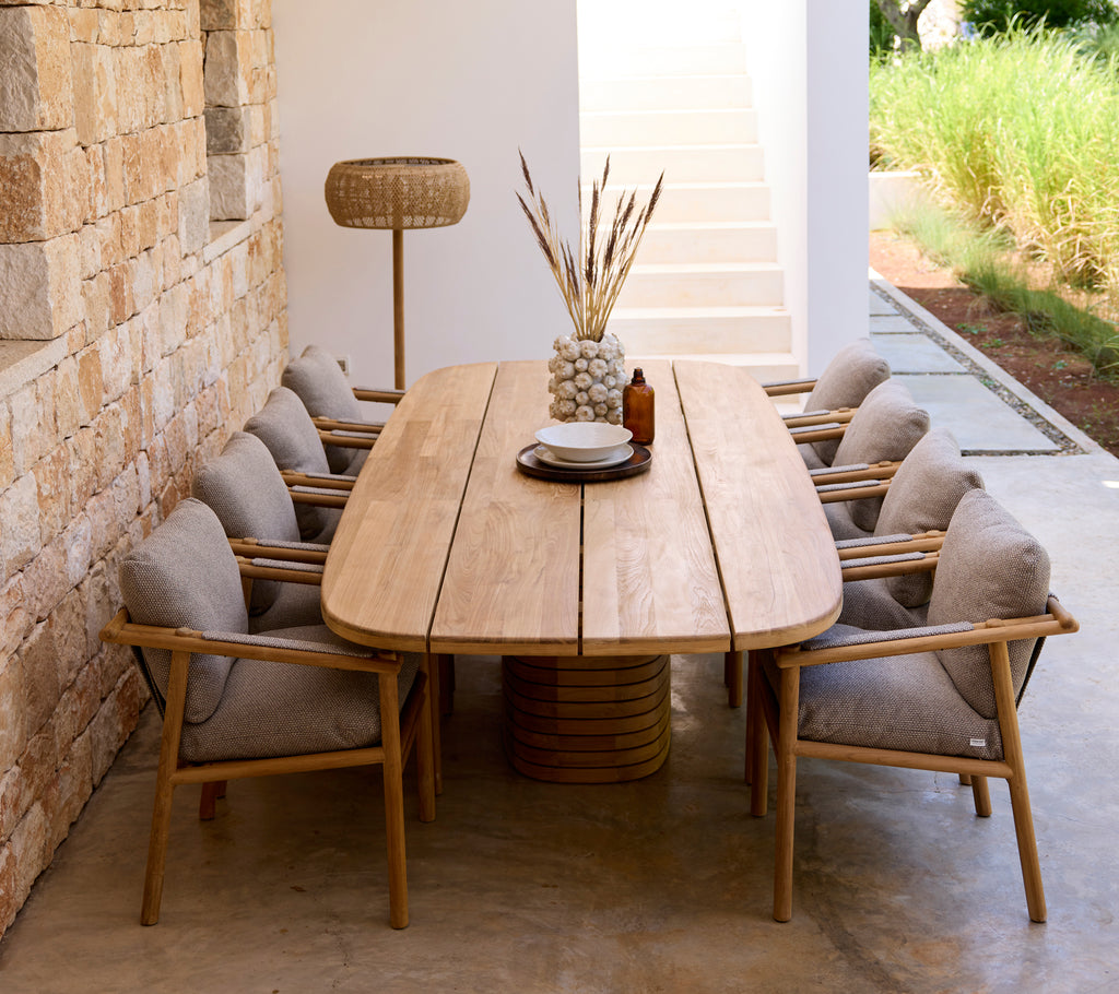 Modern matplats med träbord, grå kuddar och trästolar.