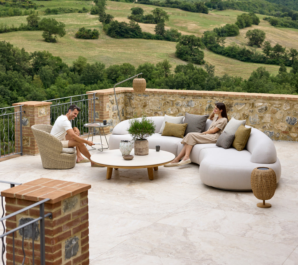 Avslappnande sittarrangemang med en mjuk lounge-soffa, Coast-lounge stol, Aspect kaffebord och Illusion Glow detaljer med en naturskön bakgrund.
