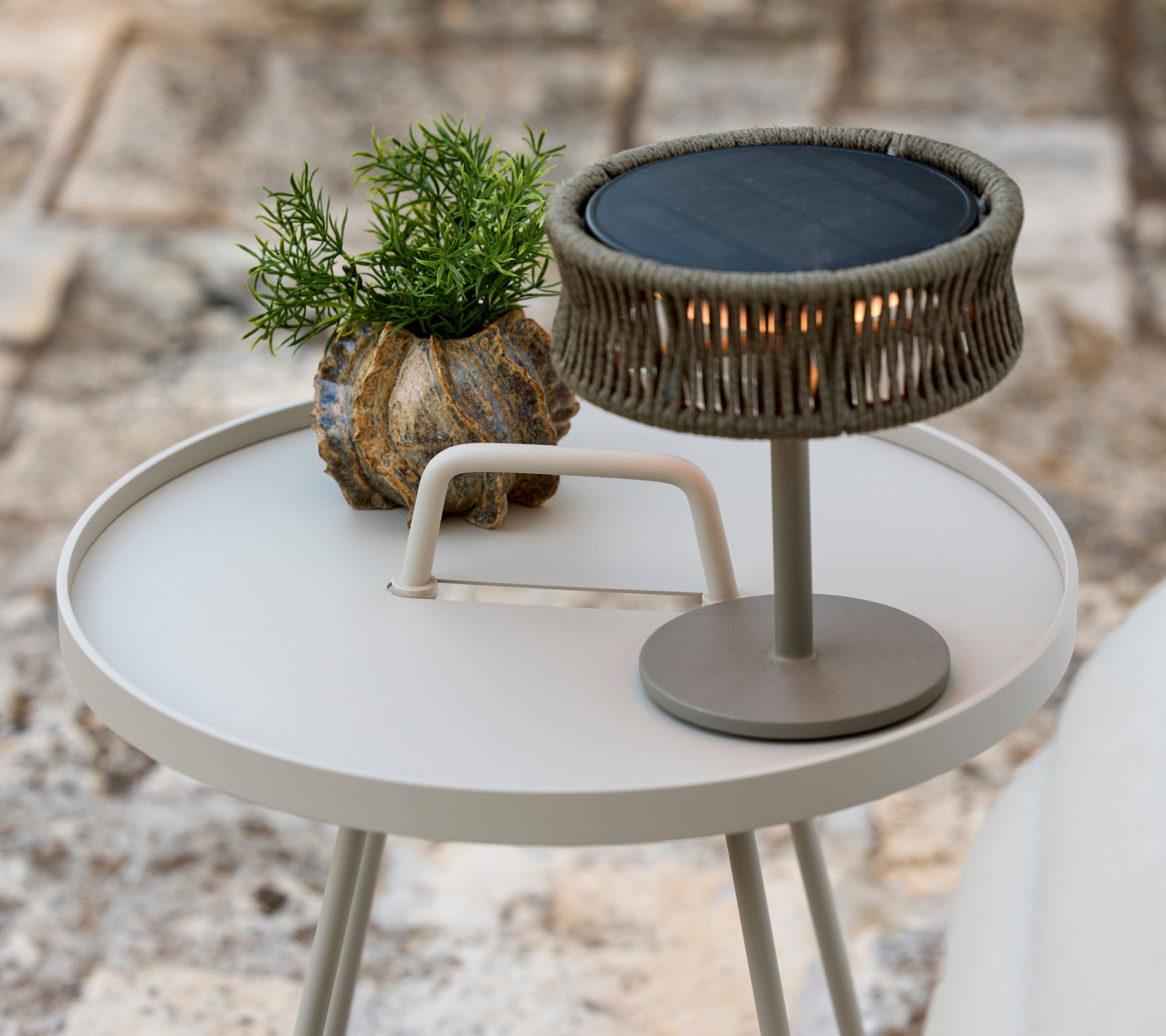 Modern grå sidobord med en grön växt och en stilren bordslampa.