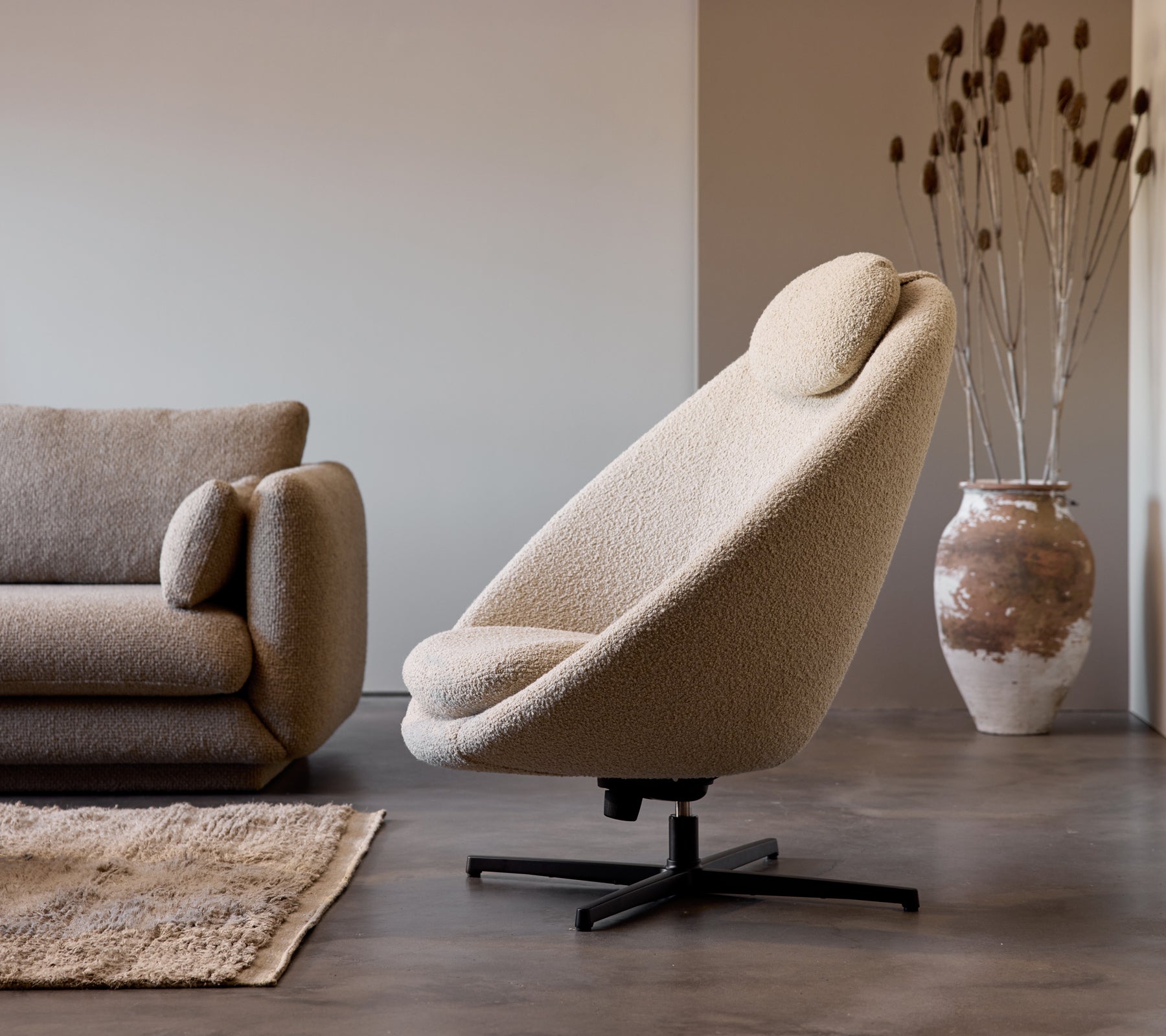 Pace fåtölj i taupe tyg bredvid en Bloom 3-sitssoffa, kompletterad med en dekorativ vas och subtil golvtextur.