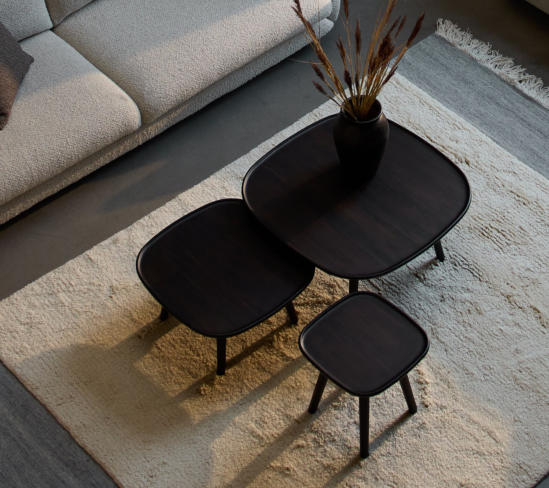 Tre stiliga Pace soffbord i varierande storlekar, med en slank design och mörk finish, åtföljt av en dekorativ vas och torkade växter.