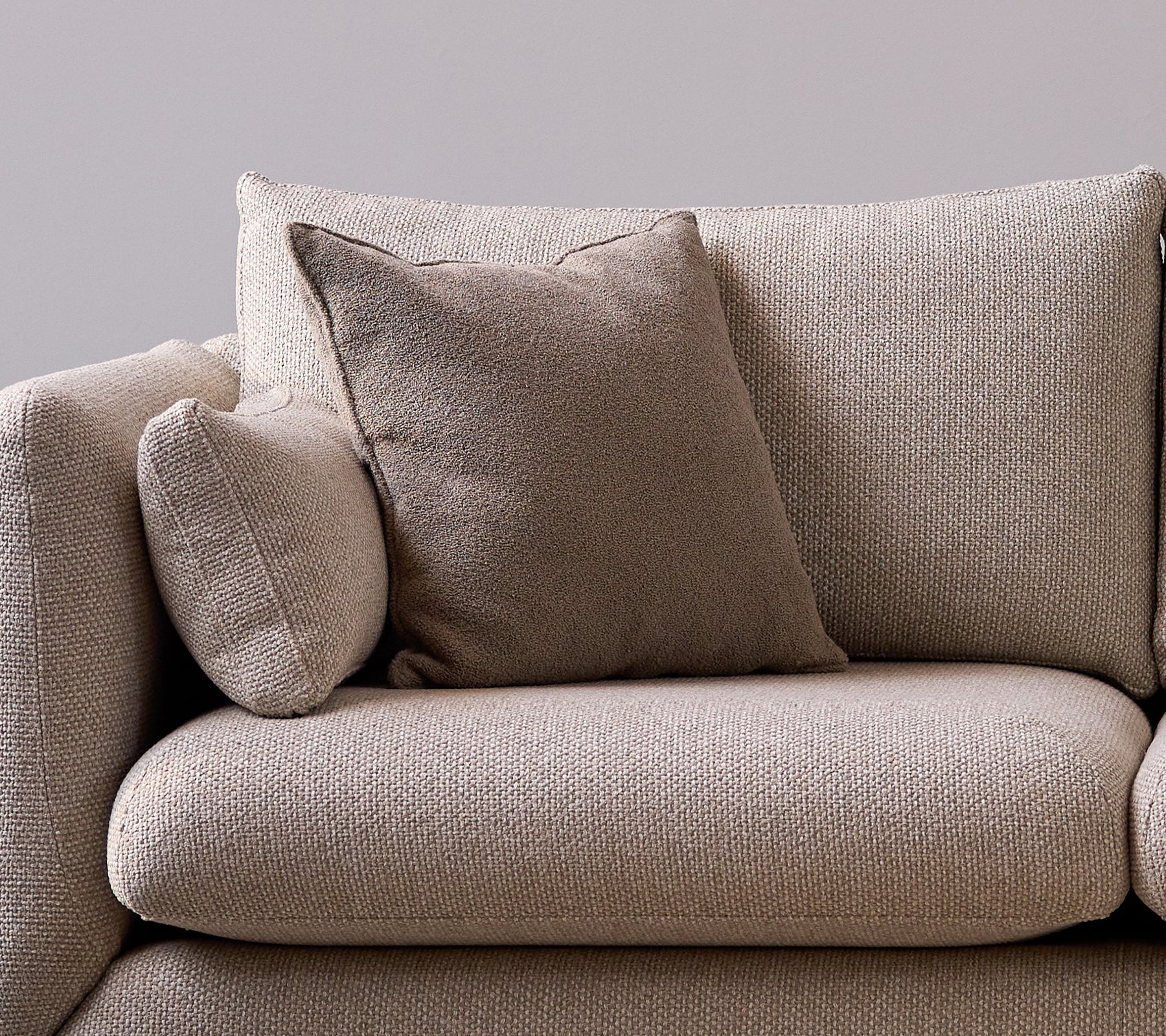 Taupe doftspridande kudde på en mjuk, texturerad soffa som ger en mysig och stilfull känsla till sittutrymmet.