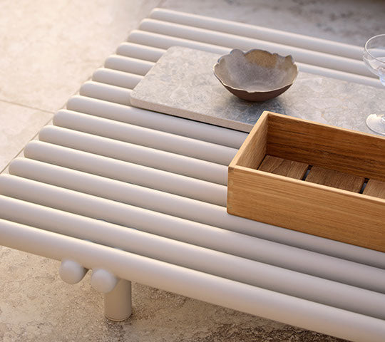Aluminum coffee table with slatted design, featuring a wooden storage box and ceramic bowl on a minimalistic surface.
