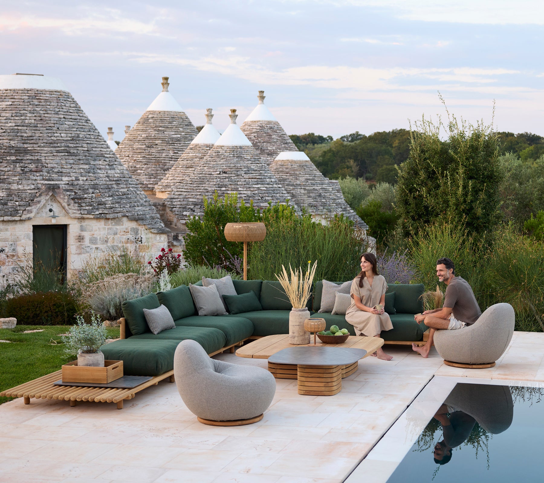 Moderna utomhuslounger med grön sektionell soffa och grå stolar vid en pool.