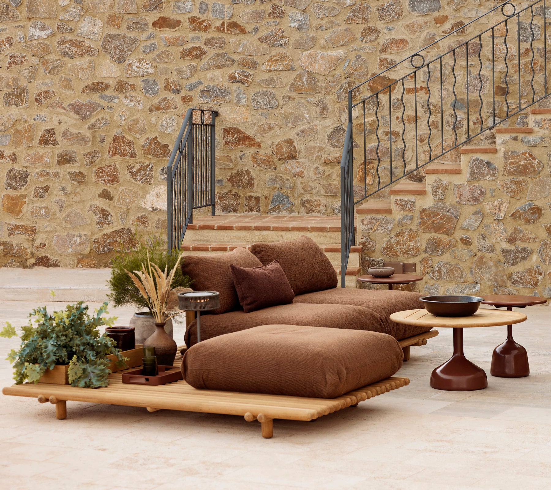 Teak-lounge med mjuka kuddar och ett Glaze soffbord, kompletterat med dekorativa växter och en texturerad stenvägg.