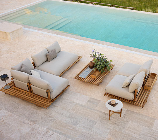 Stylish teak seating with Natte cushions, complemented by a matching coffee table and a potted plant, set beside a tranquil pool.