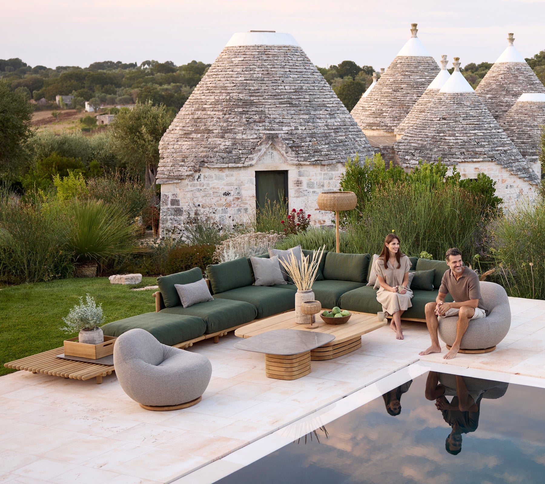 Modern utomhuslounge med en grön soffa, grå stol och runt kaffebord.