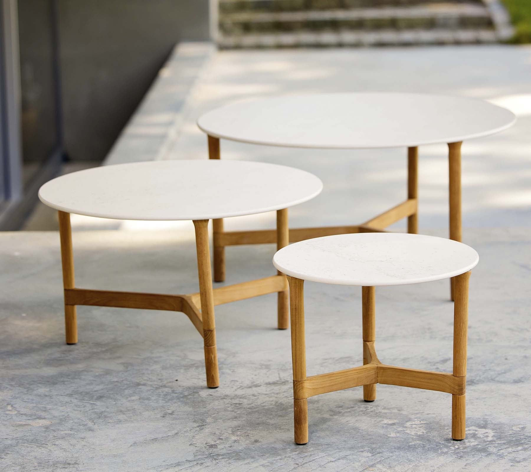 Tre moderna soffbord i olika storlekar med vita skivor och ben av trä, som visar en stilren och minimalistisk design.