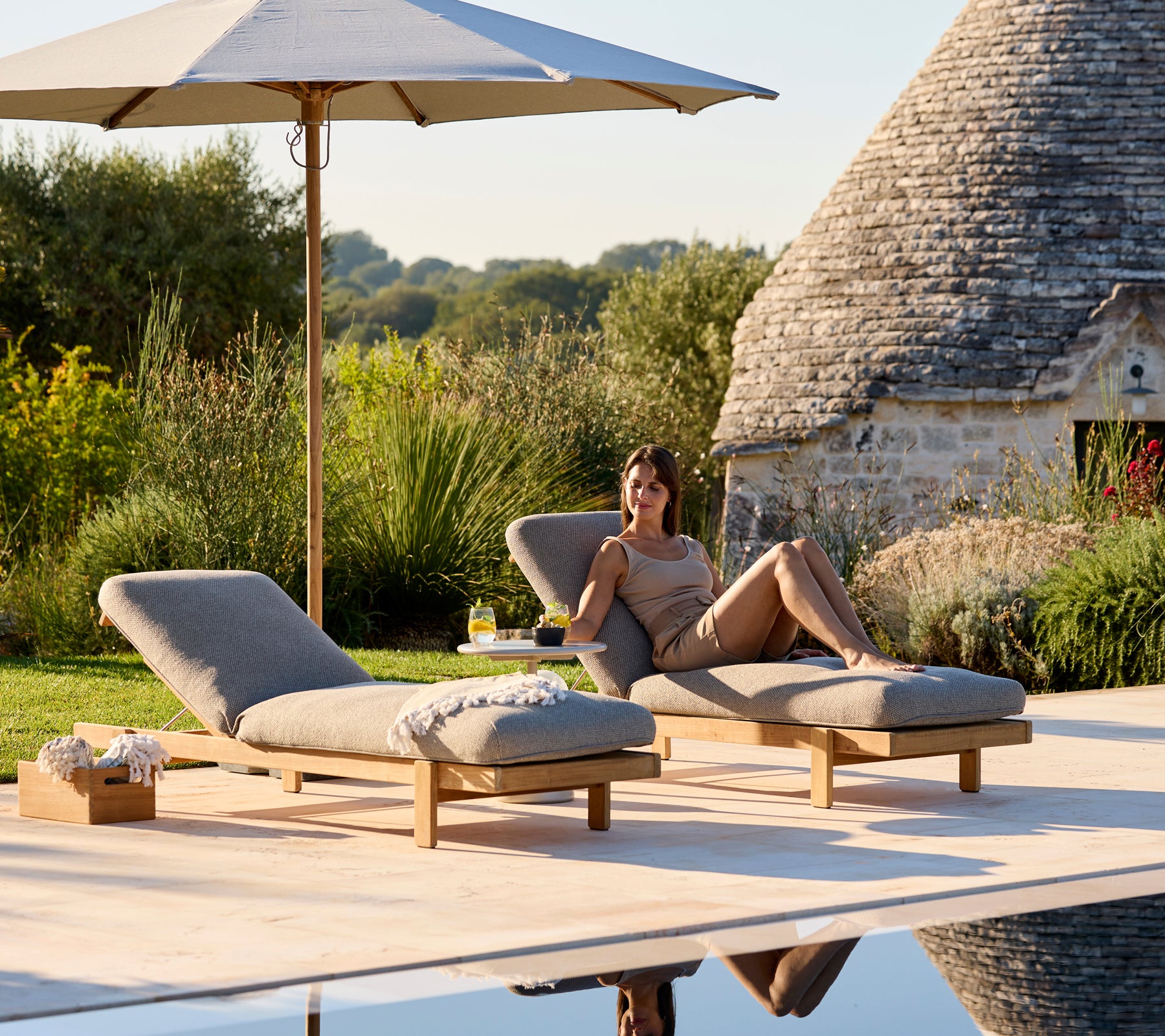 Två solstolar med beige kuddar under ett parasoll i en lugn utomhusmiljö.