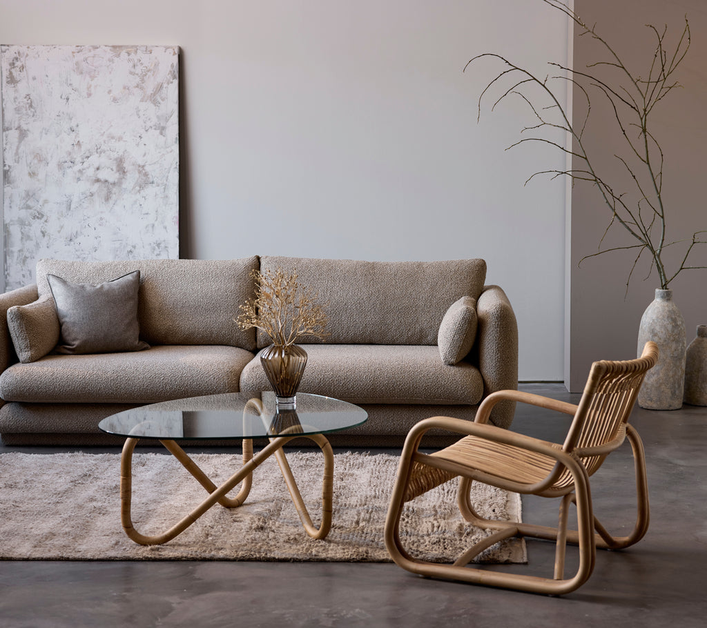 Samtida loungemöbel med en beige soffa, glasbord och vävd stol.