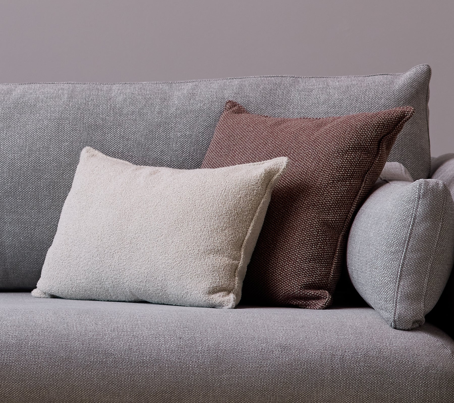 En vit Scent-kuddscatter och en Wove mörk bordeaux-kudde är placerade på en grå soffa.