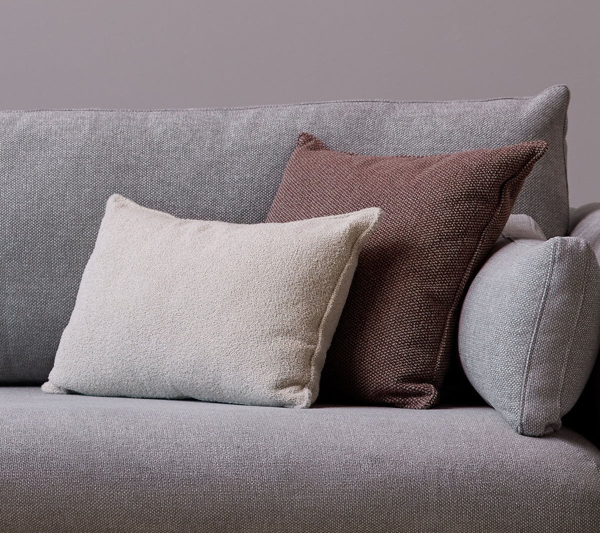 En vit Scent-kuddscatter och en Wove mörk bordeaux-kudde är placerade på en grå soffa.