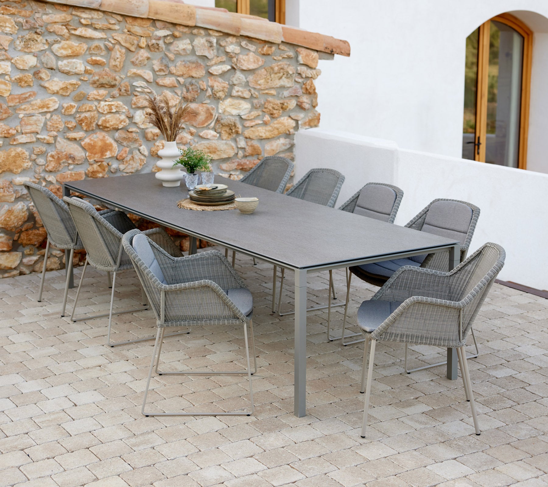 Moderna matbord med taupe stolar, dekorerat med dekorativa föremål och ett inslag av grönt mot en stenvägg.