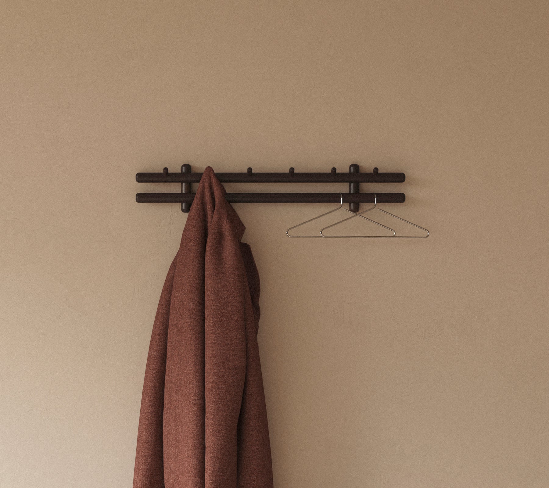 En brun kappa hänger från en minimalistisch vägghylla med krokar, kompletterad med en enkel trådgalge mot en neutral bakgrund.