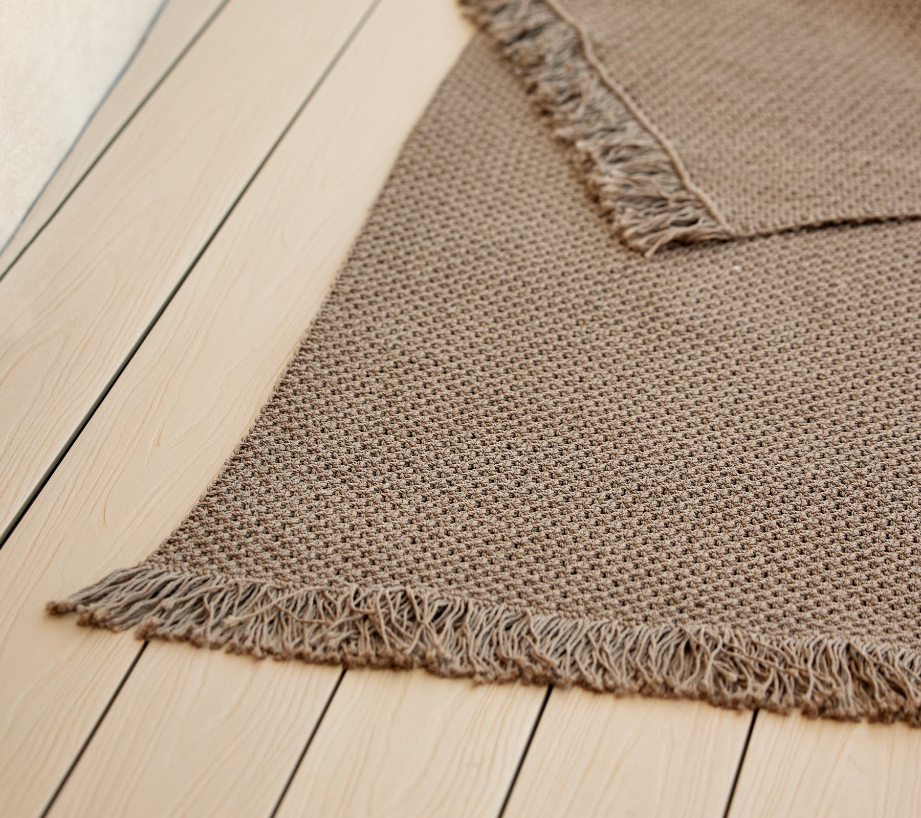 En texturerad stickad matta med fransar, som visar en varm, neutral färg som förstärker den mysiga estetik.